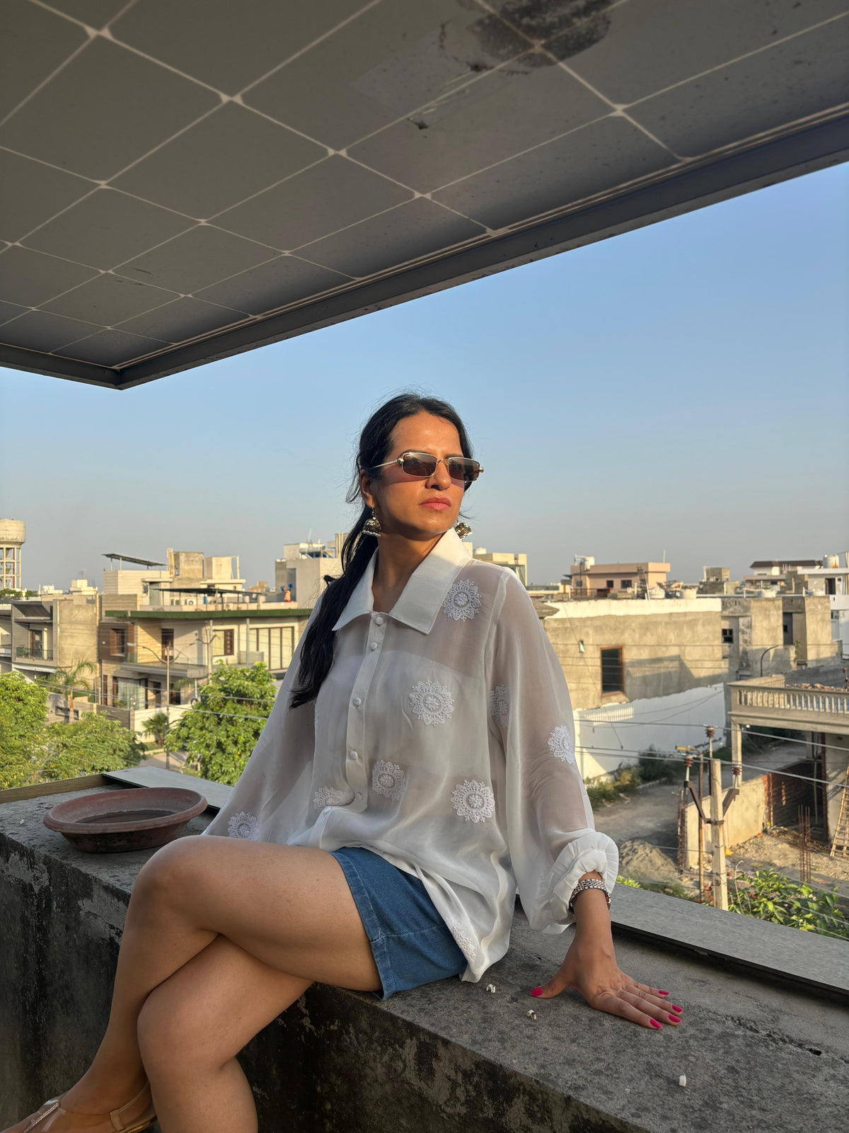 Rooh off-white Chikankari oversized shirt — lifestyle sitting on fence view, styled with shorts, everyday wear